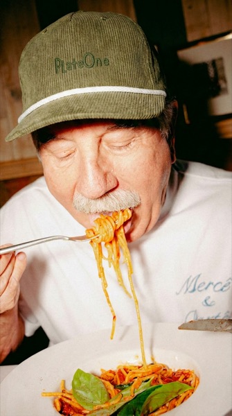 Un homme avec une casquette PlateOne mange des spaghettis à la sauce tomate.